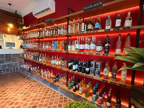 Pared roja de la tienda IVIN con anaqueles iluminados de raicilla, mezcal, tequila y otros destilados